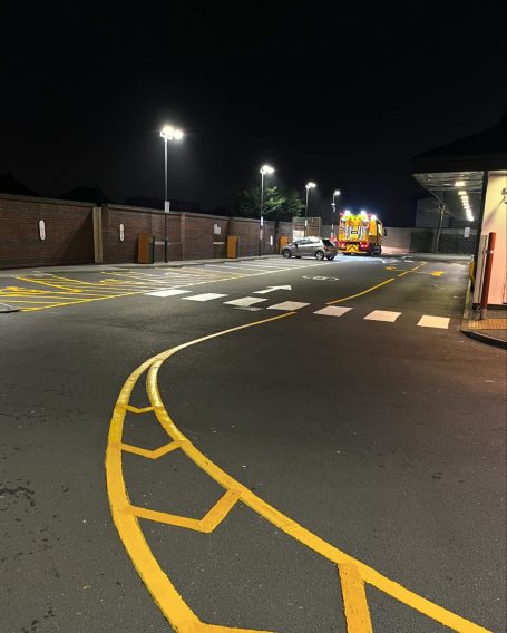 Nighttime view of a curved road with parking spaces and lighting in a commercial area.