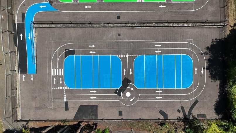 Aerial view of two blue tennis courts surrounded by green spaces.