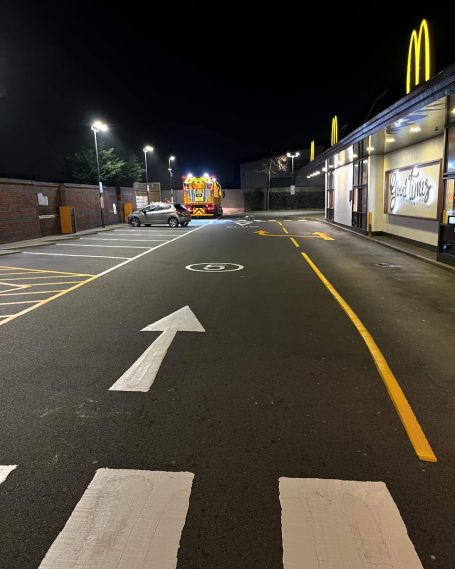 Nighttime view of a McDonald's drive-thru with clear road markings and vehicles.
