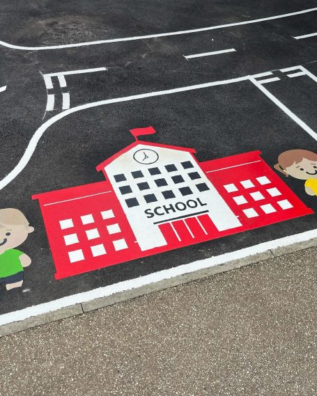 Colourful school building mural with children on a playground surface.