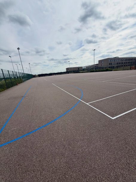 Empty outdoor sports court with blue and white markings under a cloudy sky.