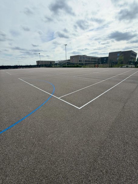 A wide view of a sports court with blue lines and a cloudy sky in the background.
