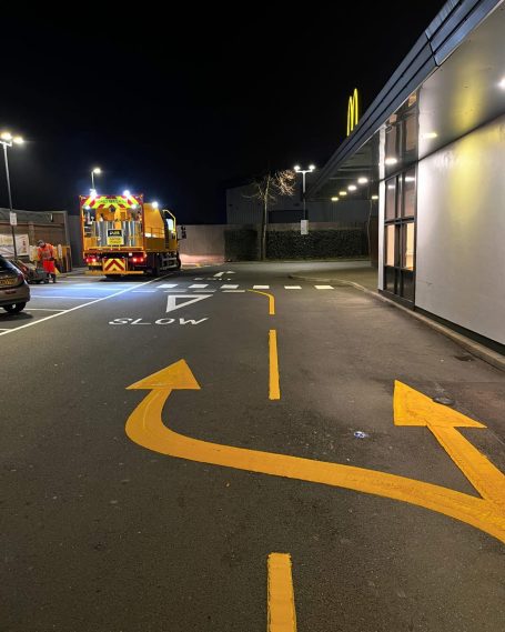 A van is parked near a road with yellow directional arrows at night.