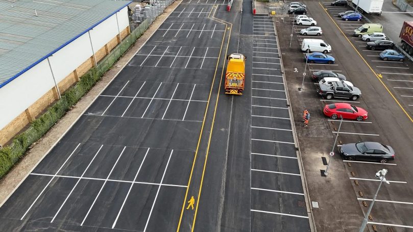 Aerial view of an empty parking lot with a yellow van and parked cars.
