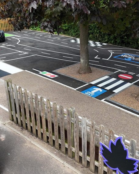 A painted street scene featuring road markings, a tree, and a wooden fence.
