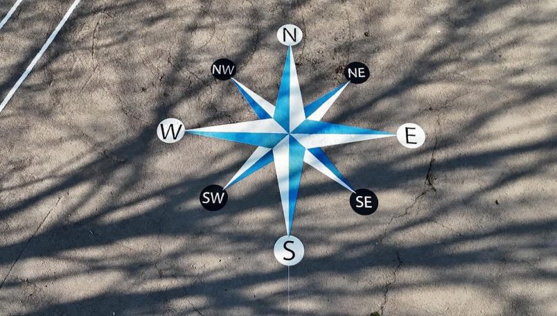 Blue and white compass rose with cardinal directions painted on a surface.