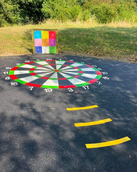 Colourful circular dartboard on pavement with three yellow lines marking throwing distance.